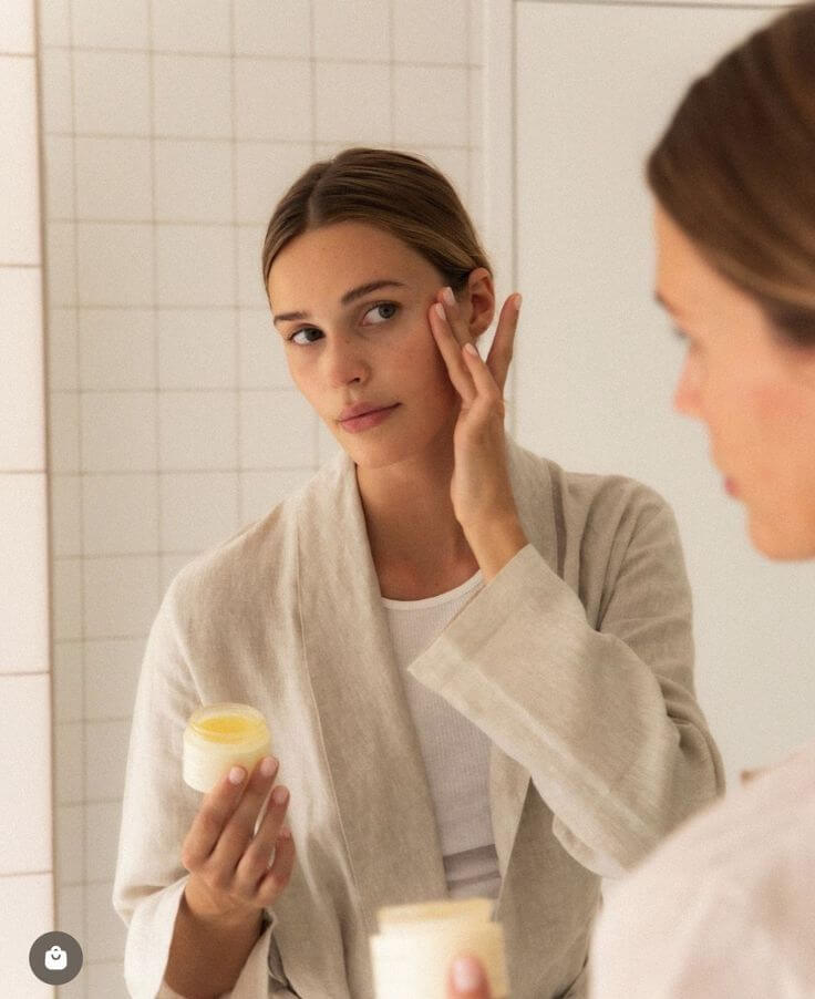 Frau benutzt Body Butter für ihre Hautpflege im Badezimmer, strahlendes Gesicht und entspannte Atmosphäre.